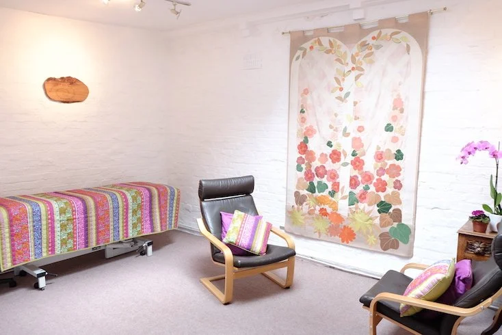 The consulting room at Violet Hill Studios, with armchairs, a therapy couch and a floral wall hanging